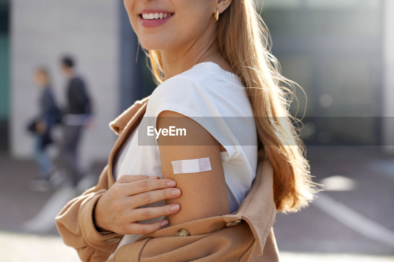 Young beautiful healthy woman showing shoulder with plaster, concept of vaccination