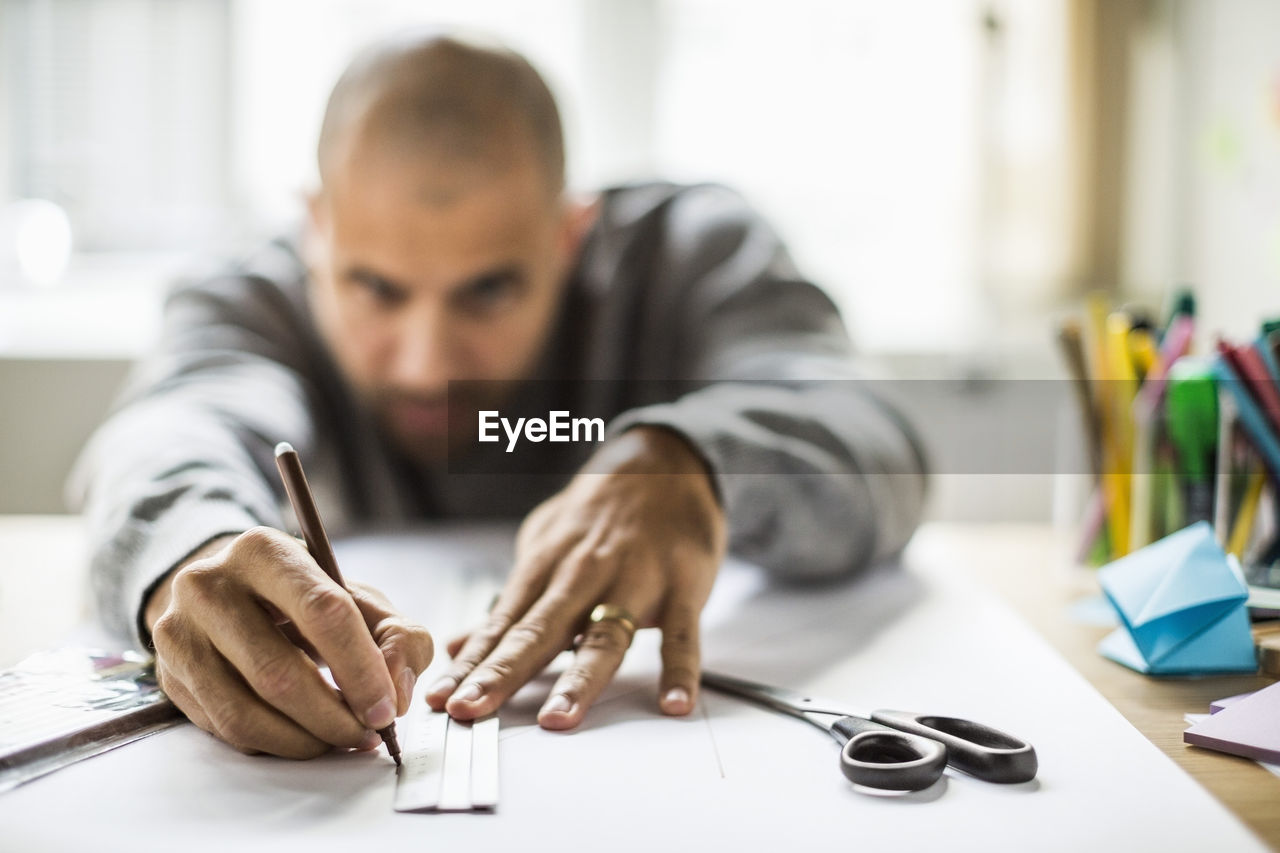 Mature businessman drawing line on paper at desk in creative office