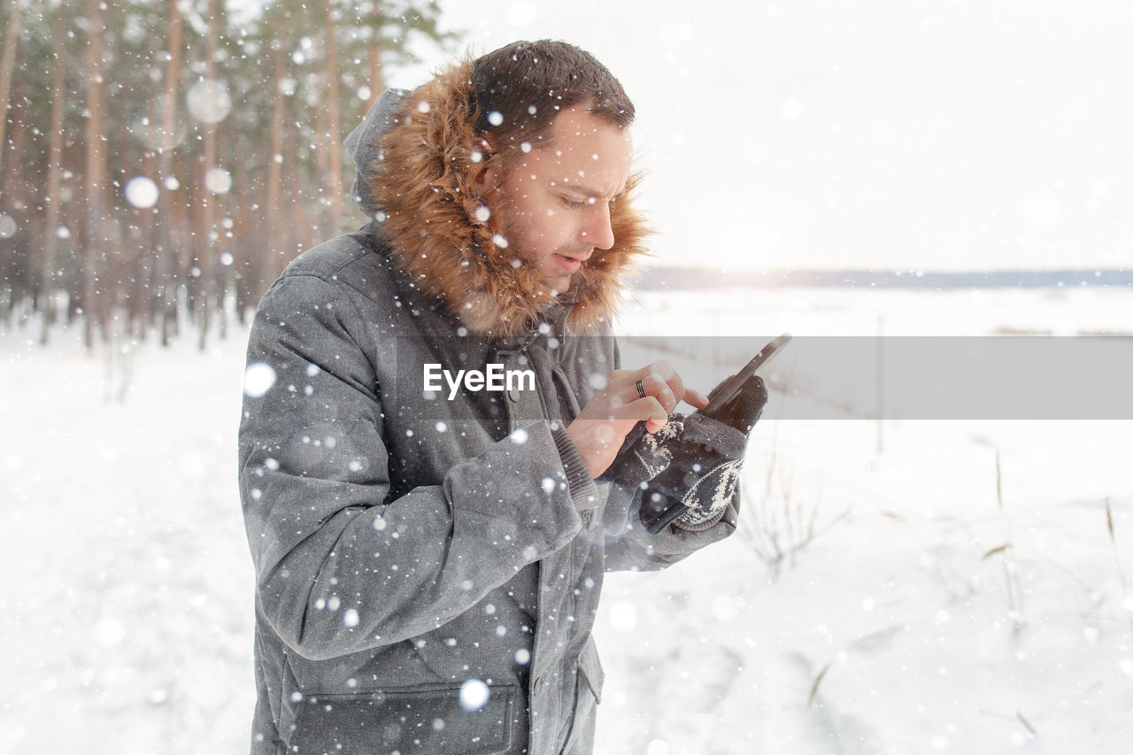 Mid adult man using smart phone on snow covered field