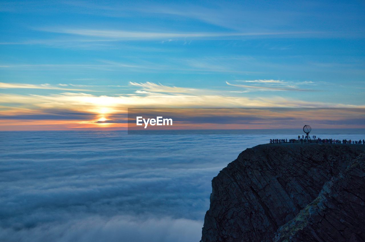 Silhouette people standing on cliff against sky during sunset