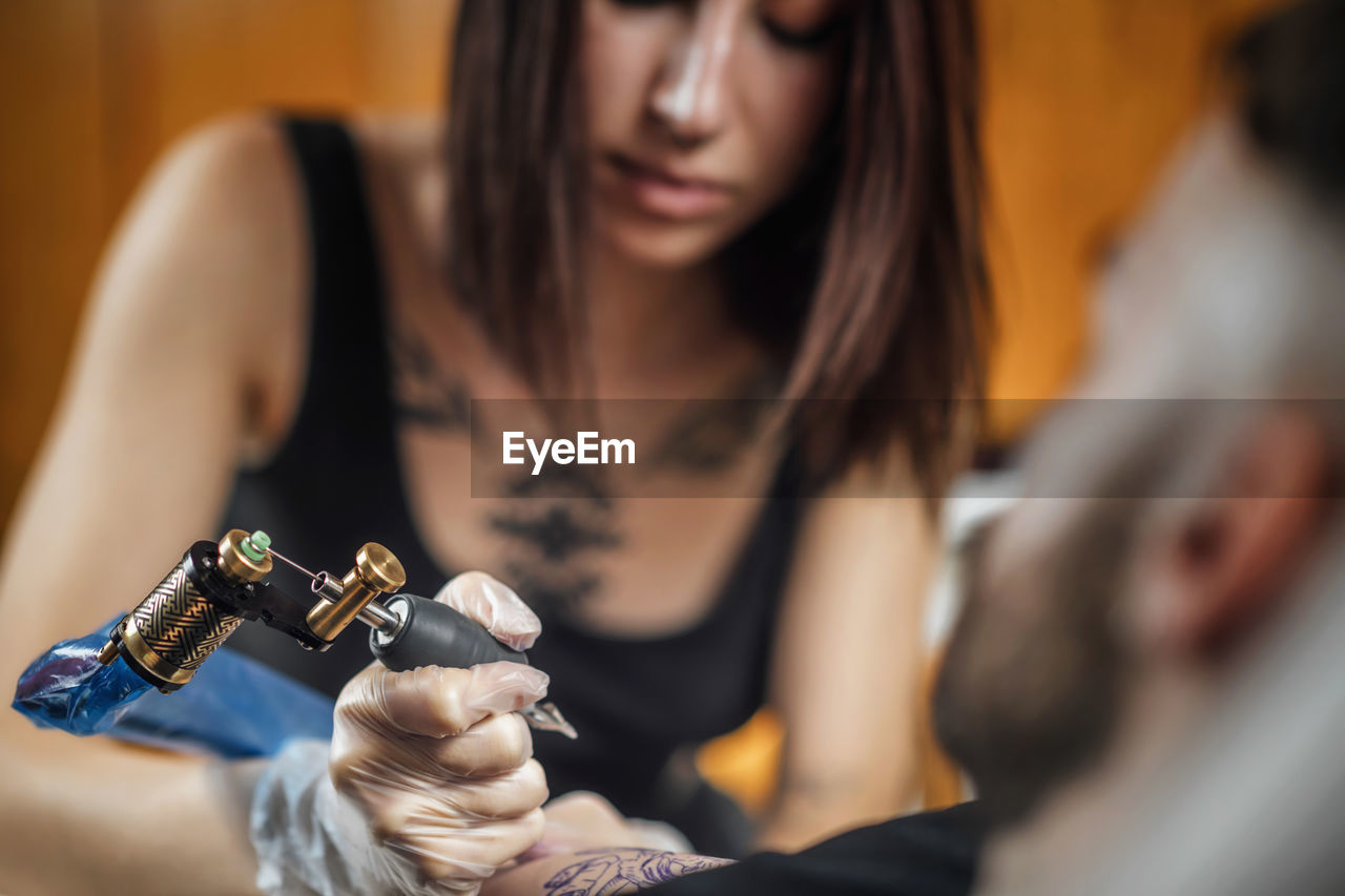 Female tattoo artist tattooing mans arm in studio