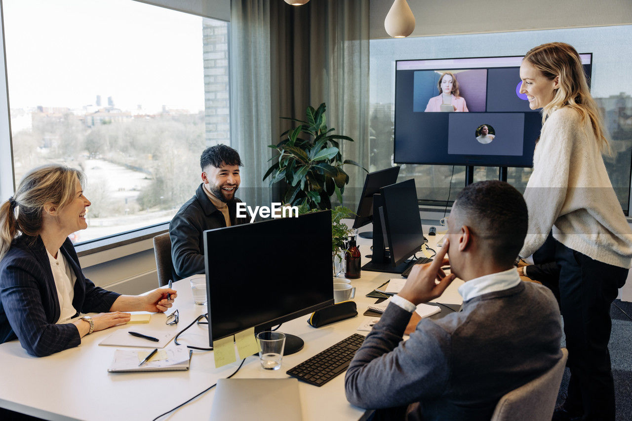 Happy business colleagues discussing with each other in conference room at office