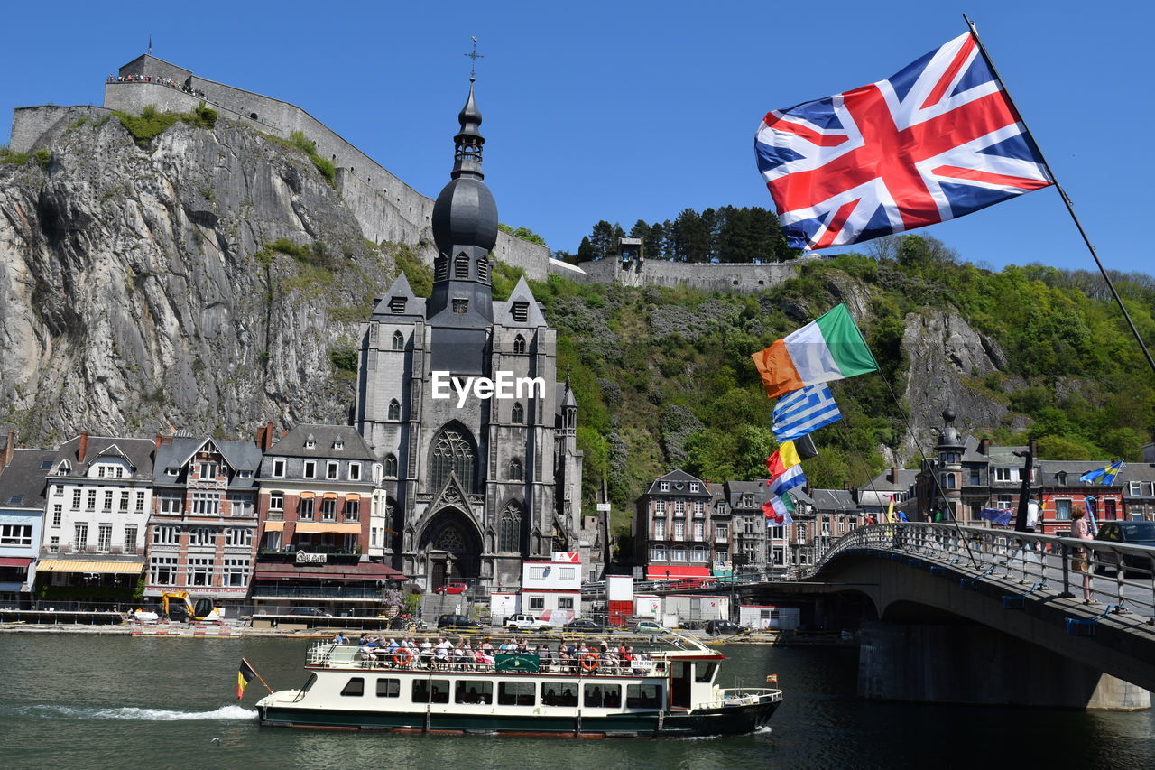 Ferry sailing in river by notre dame de dinant against sky