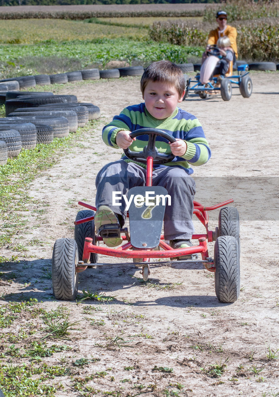 Little boy races others around a track on a peddle car at a fall festival