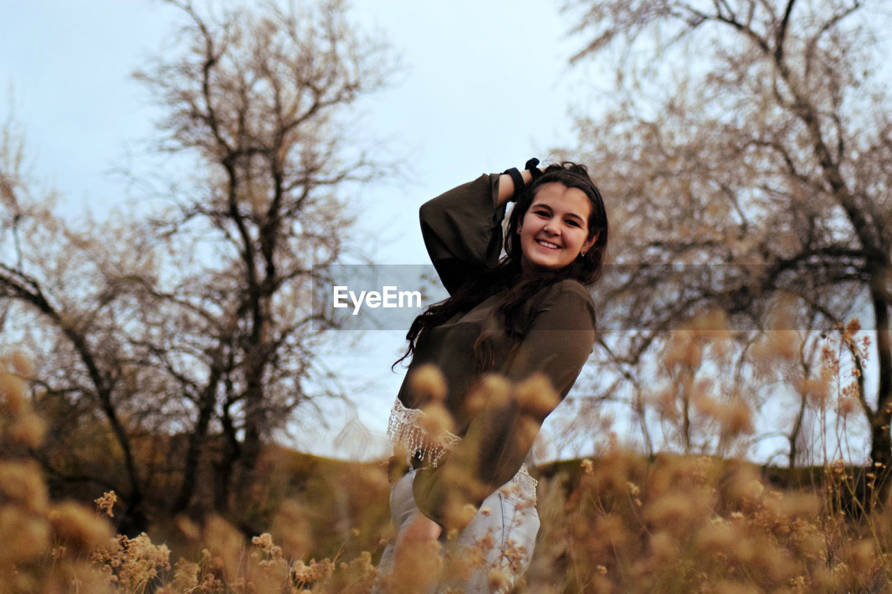 Cheerful young woman posing on field during autumn