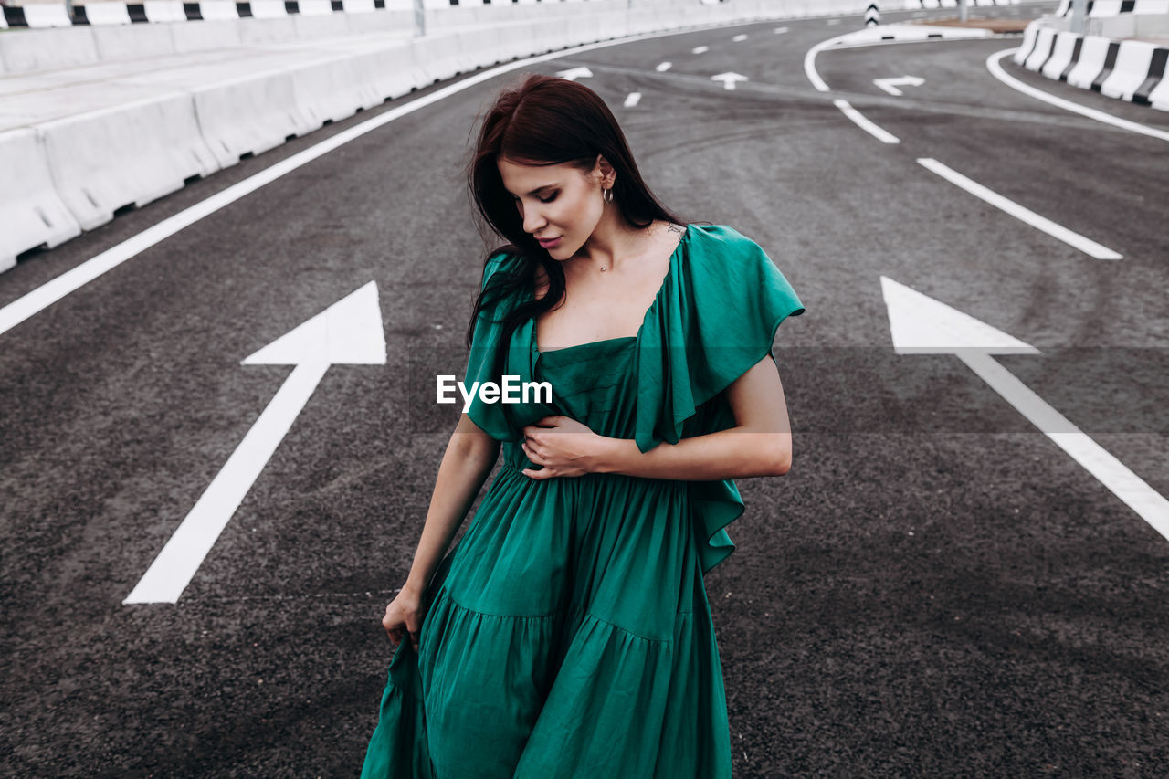 FULL LENGTH OF A YOUNG WOMAN STANDING ON ROAD