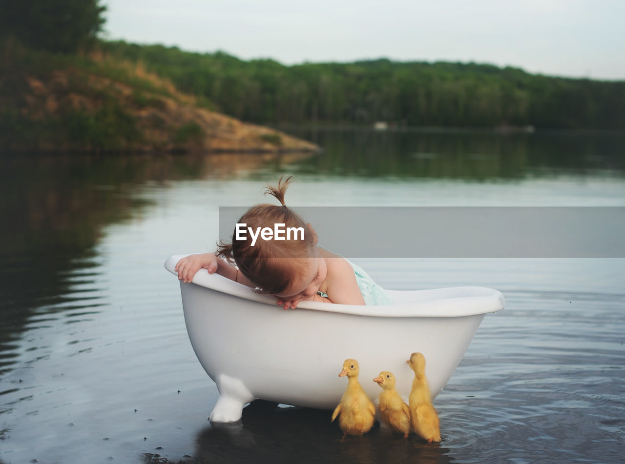 Little baby girl in a bathtub in the lake with three ducklings