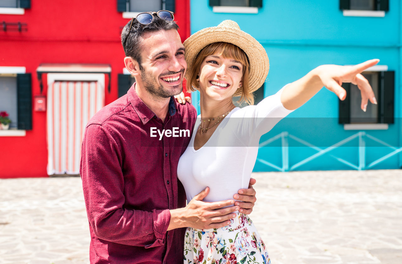 HAPPY FRIENDS SMILING WHILE STANDING AGAINST BLURRED BACKGROUND