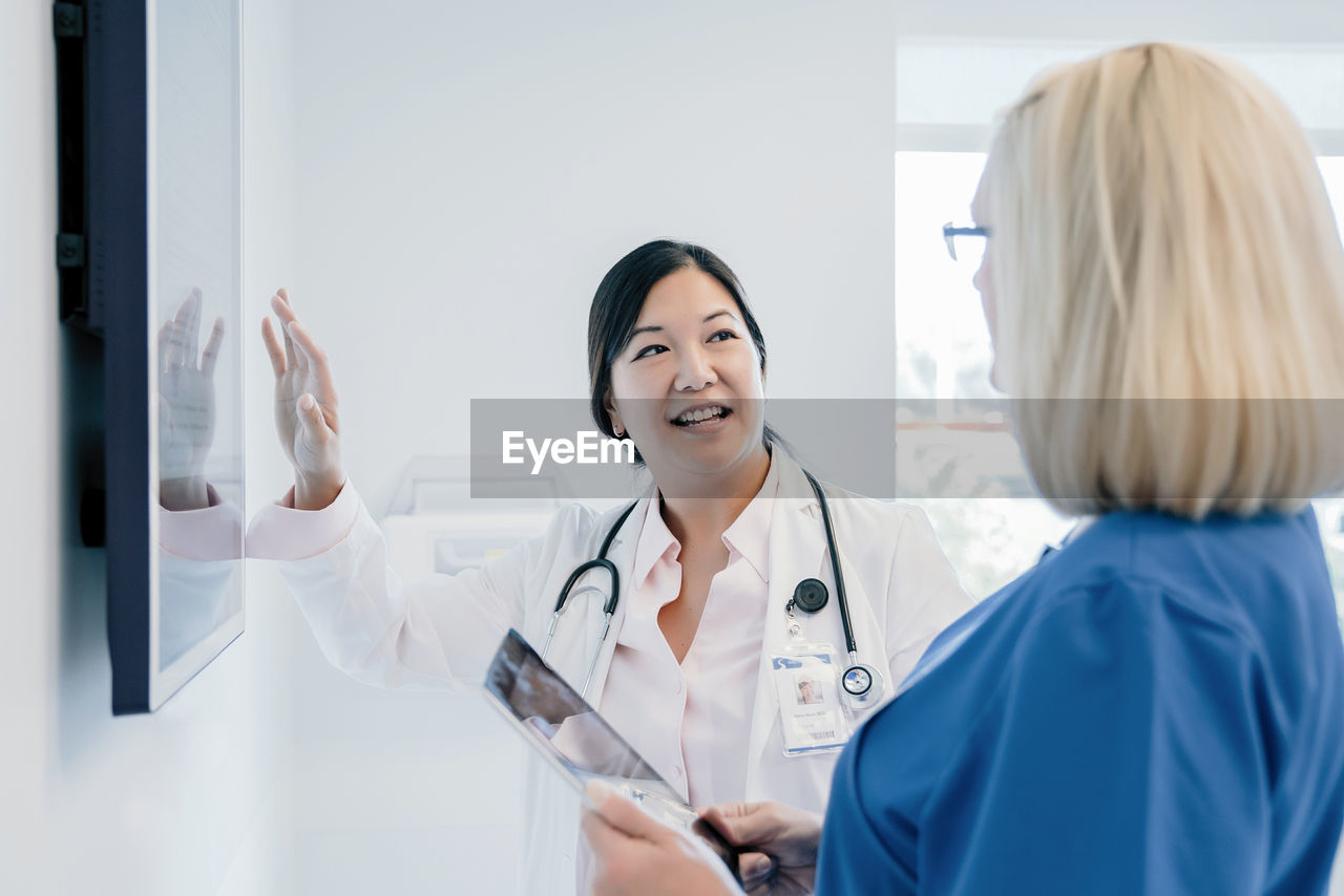 Female doctor gesturing at flat screen while discussing with colleague in hospital