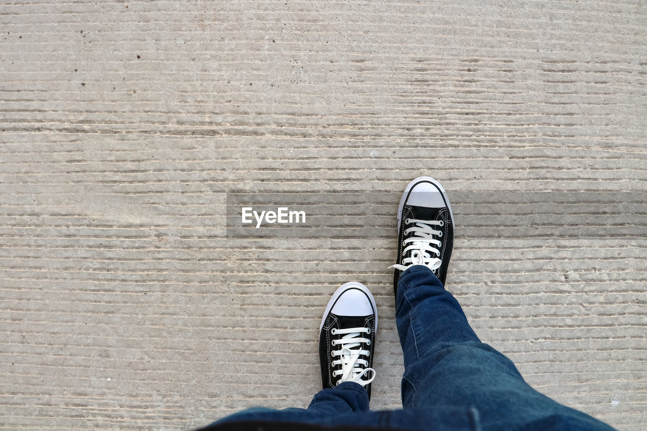 low section, shoe, human leg, one person, blue, personal perspective, white, lifestyles, standing, jeans, casual clothing, men, sneakers, black, limb, human limb, canvas shoe, footwear, leisure activity, high angle view, day, directly above, spring, walking shoe, outdoors, skate shoe, adult, human foot