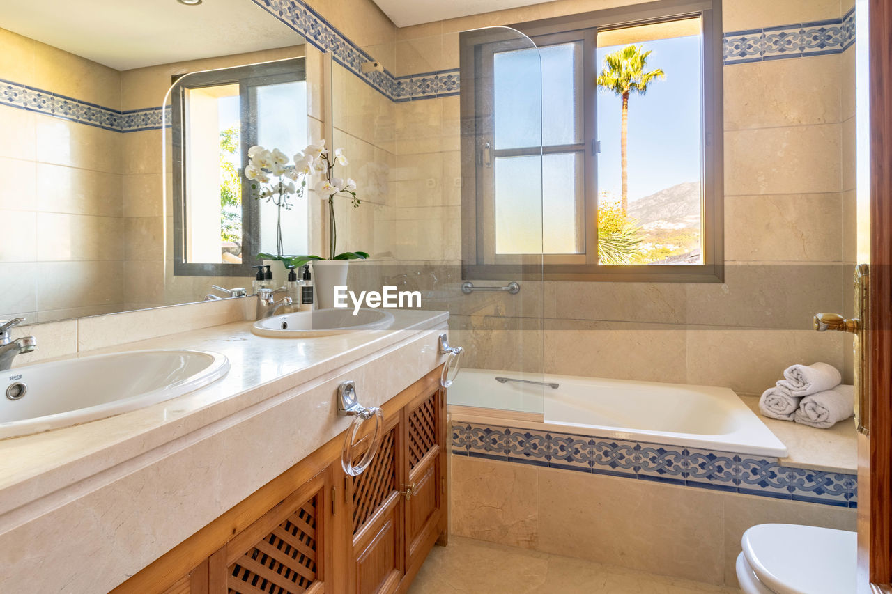 A image of a bathroom with a double sink with views overlooking a palm tree and mountain of marbella