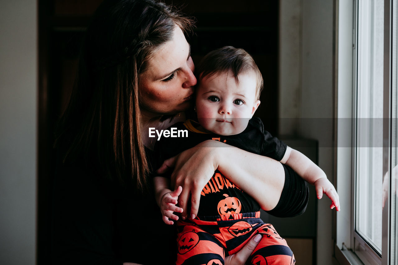 Portrait of daughter with mother sitting by window at home