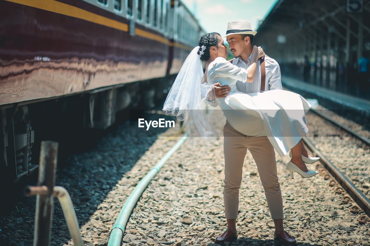 Groom carrying bride and looking at each other while standing on rail road track