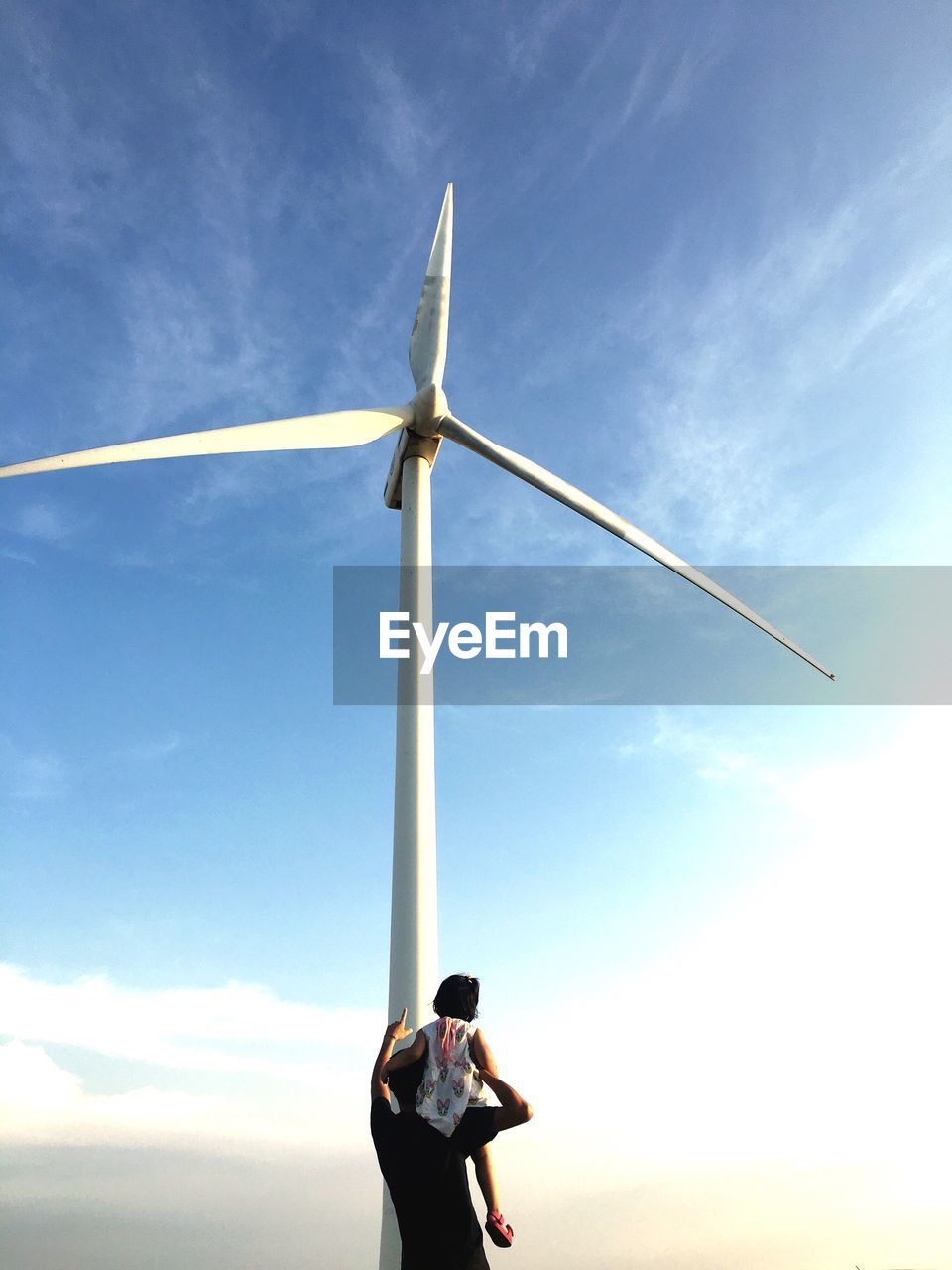 Father showing windmill to daughter against sky