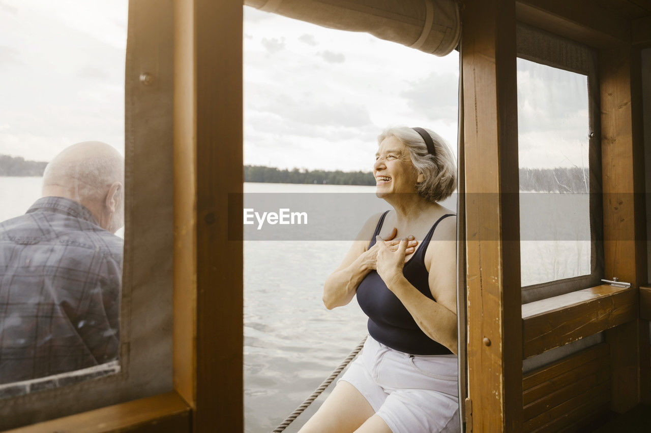 Happy senior woman with hands on chest sitting near man at houseboat