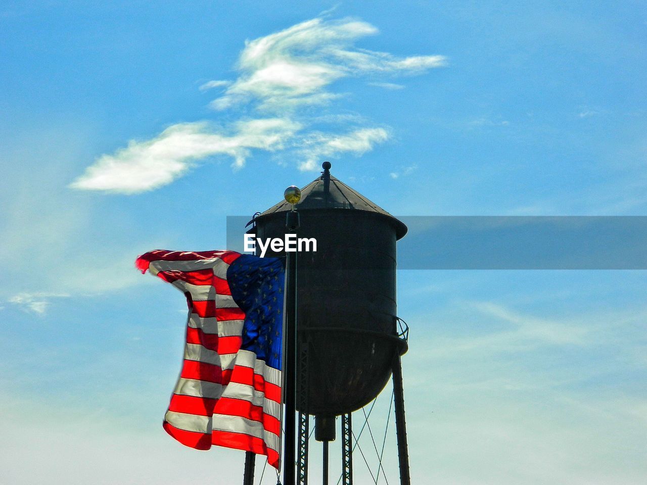 Low angle view of water tank and american flag against blue sky