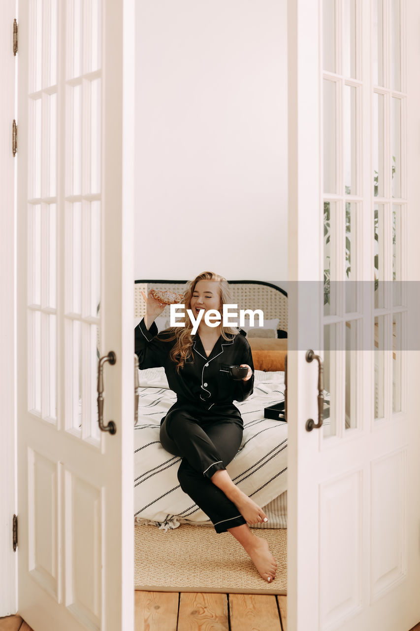 PORTRAIT OF YOUNG WOMAN SITTING AT ENTRANCE OF HOME