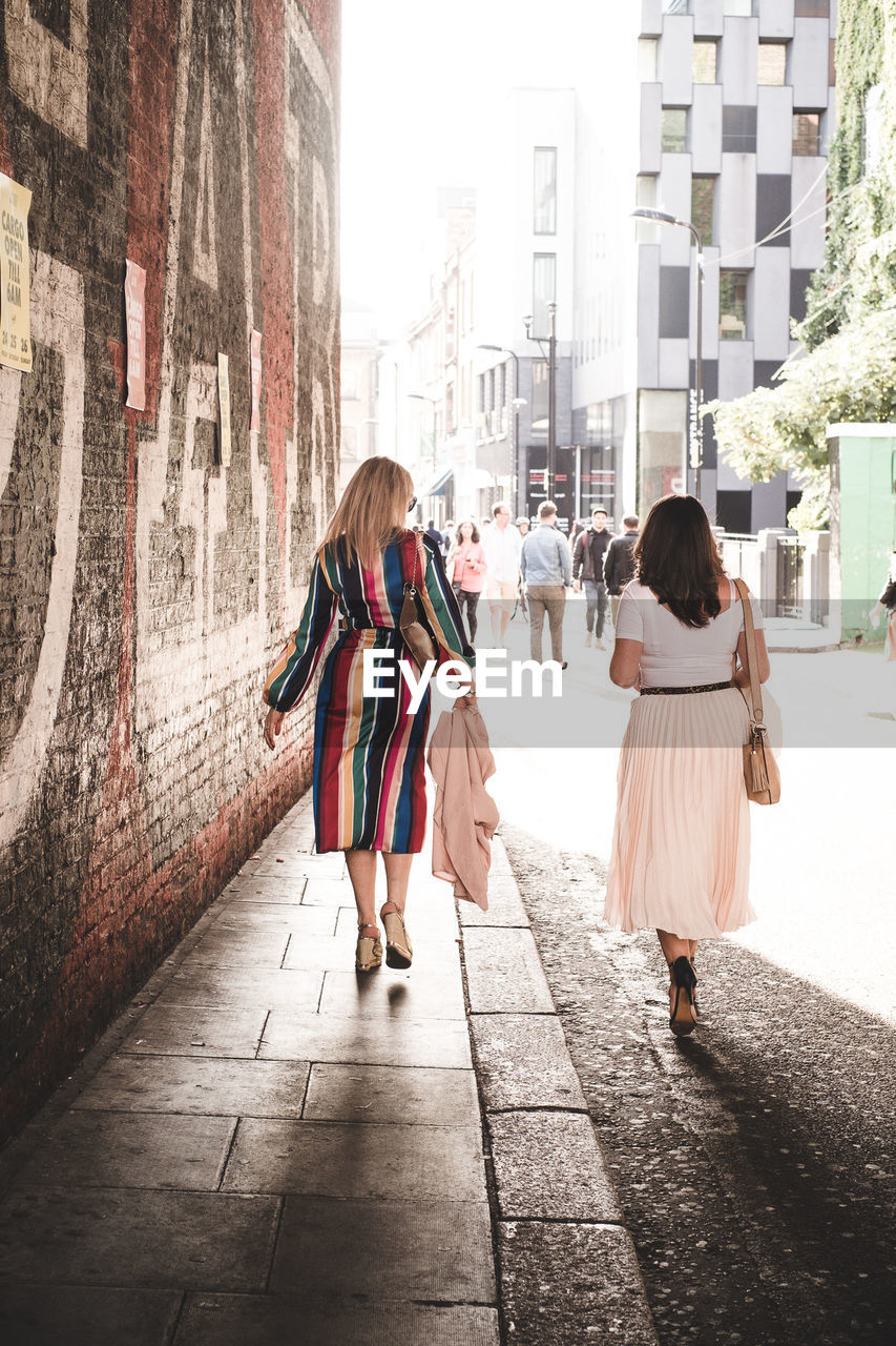 Rear view of women walking on footpath in city