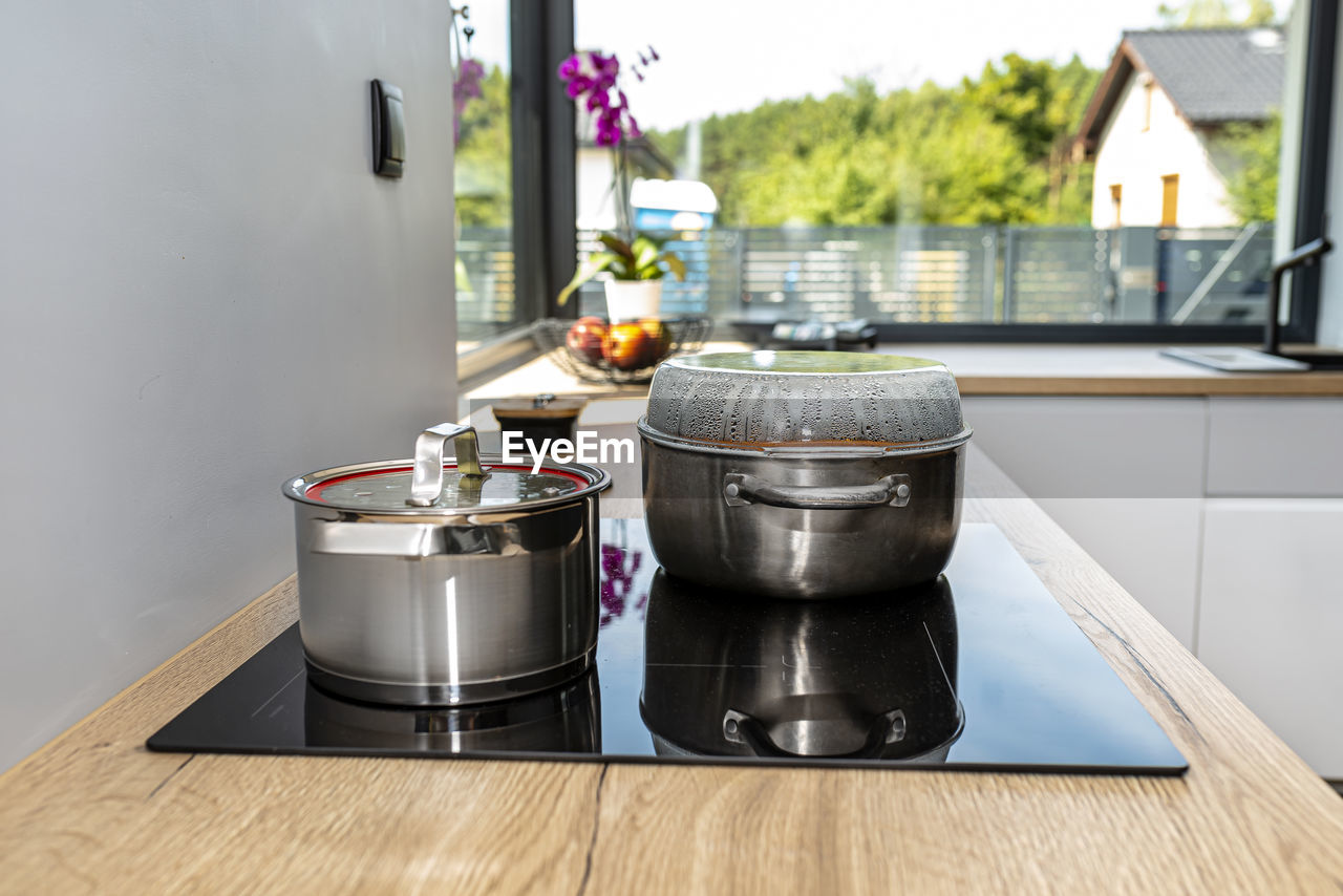 Steel pots with a cooking dish on an induction cooker built into the kitchen worktop on the cabinets