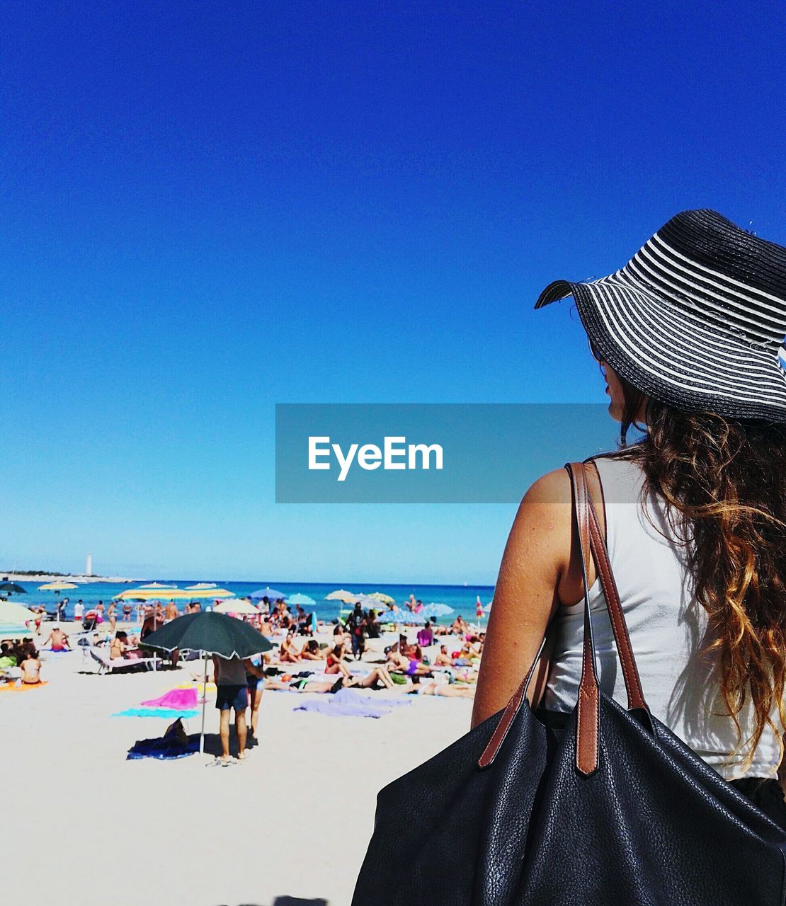 Woman in hat standing at beach against clear blue sky during sunny day