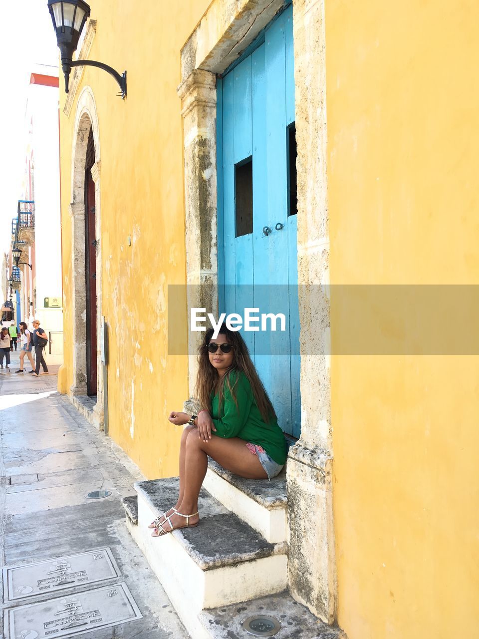 Full length portrait of woman sitting at entrance of building