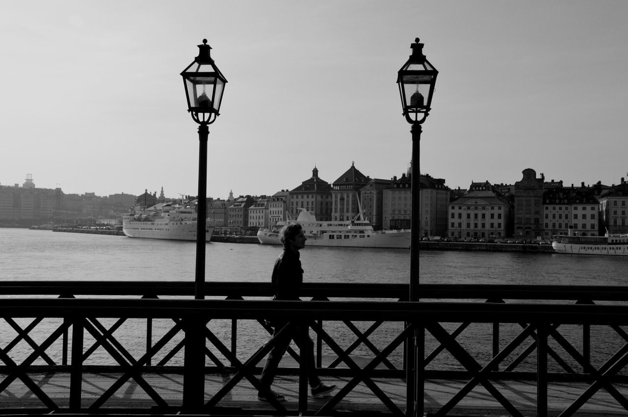 Silhouette man walking on footbridge with city in background