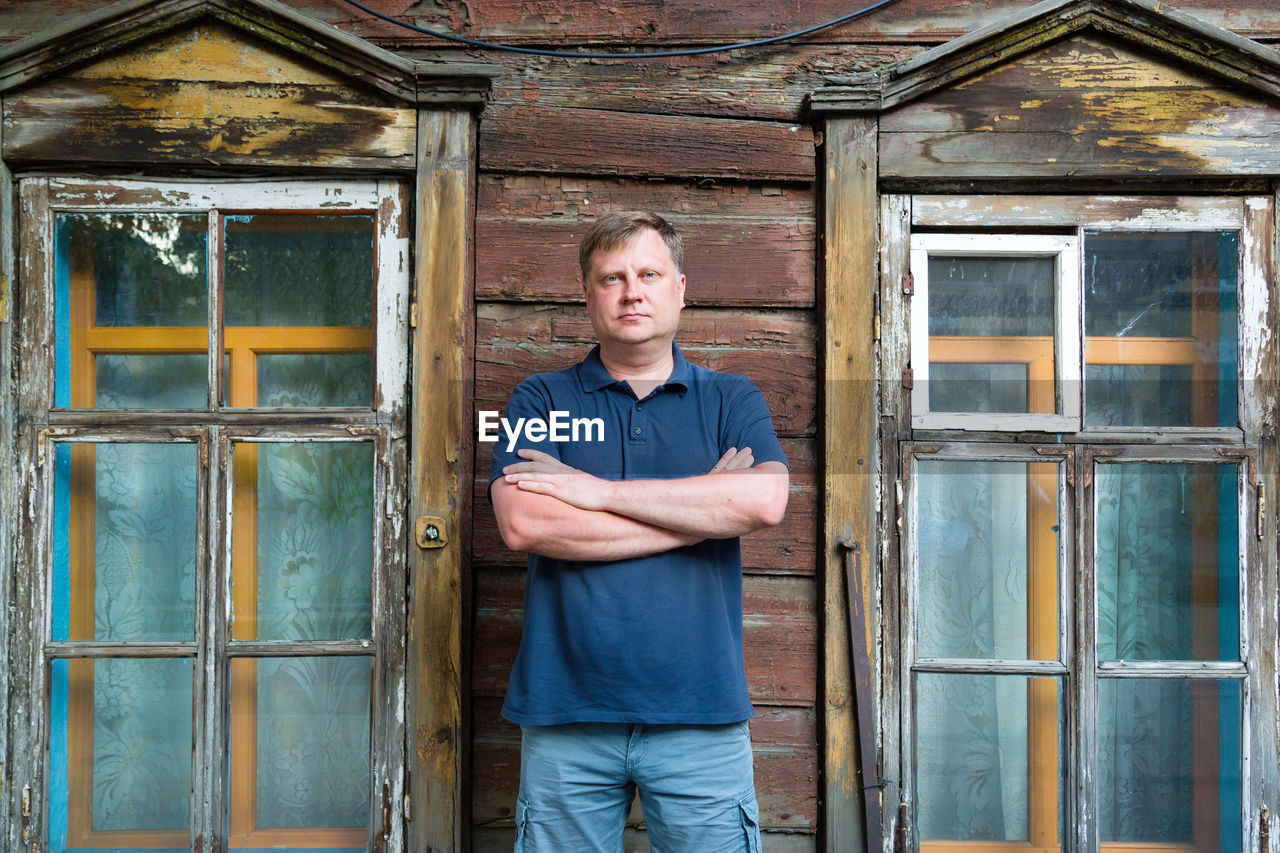 An adult man stands at wooden abandoned building.