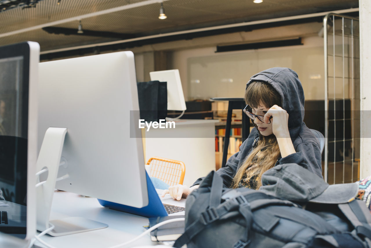 Female computer programmer using laptop while looking over eyeglasses in office