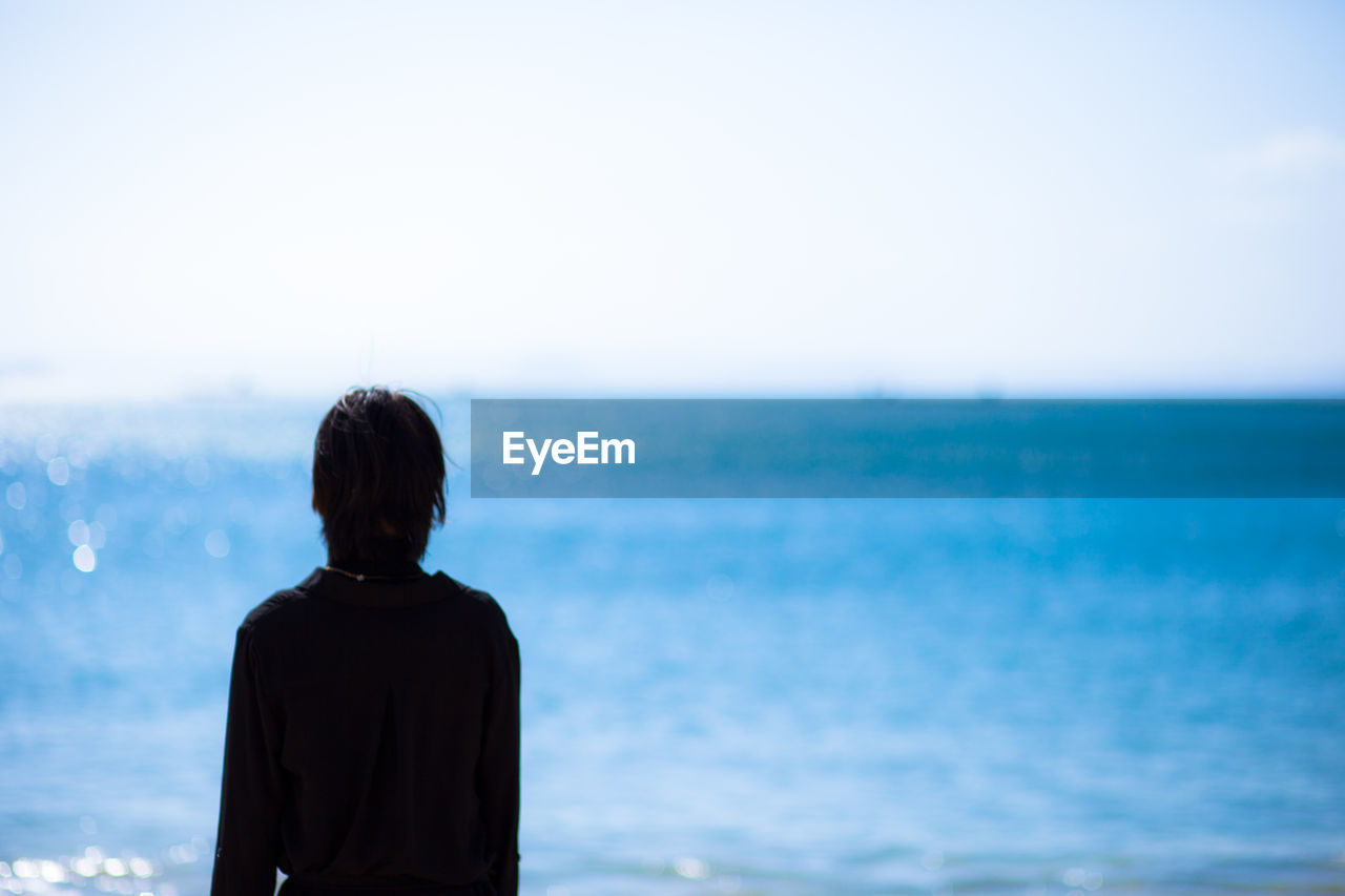 REAR VIEW OF MAN STANDING AGAINST SEA