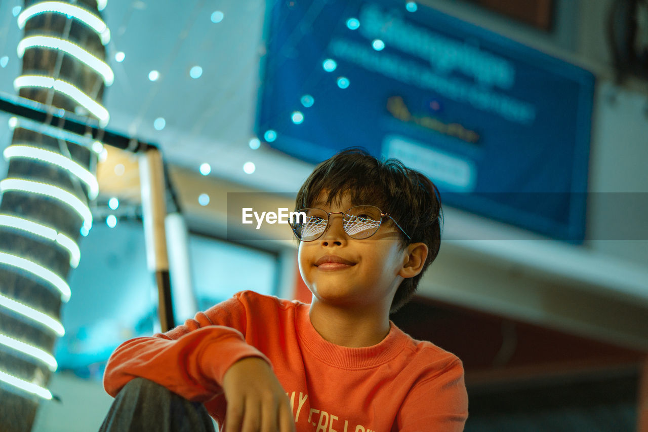 Low angle view of cute boy wearing eyeglasses against illuminated building at night