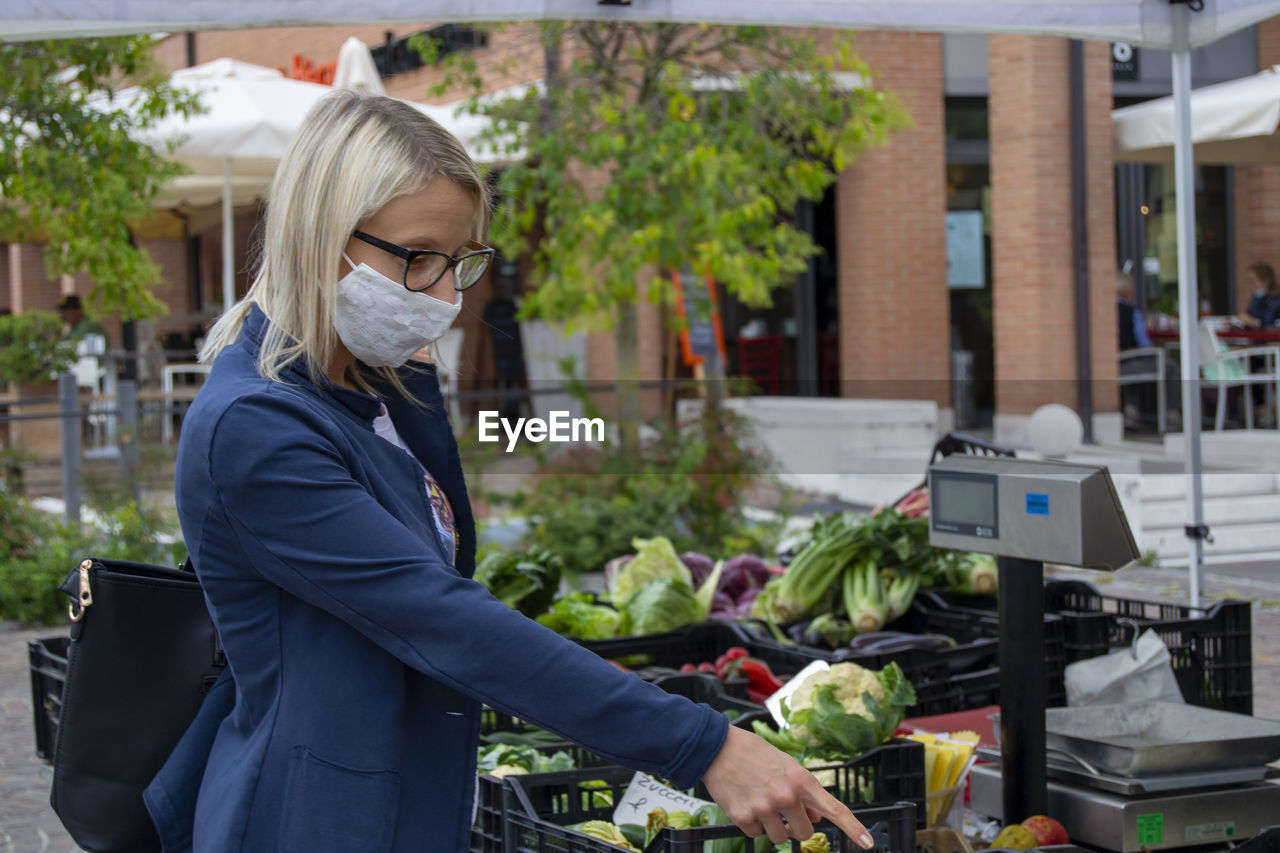 Women with mask at farmer's market, buying vegetables.