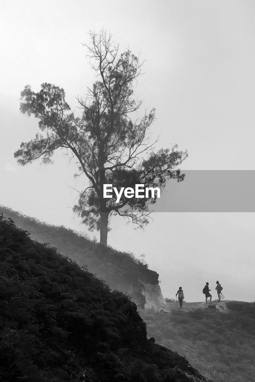 Three hikers standing on mountain against clear sky