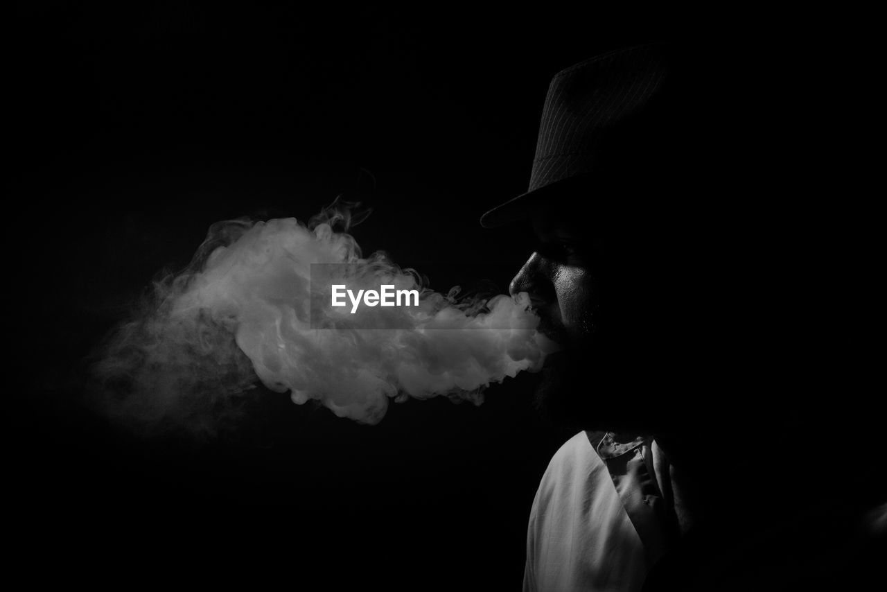 Side view of man smoking against black background