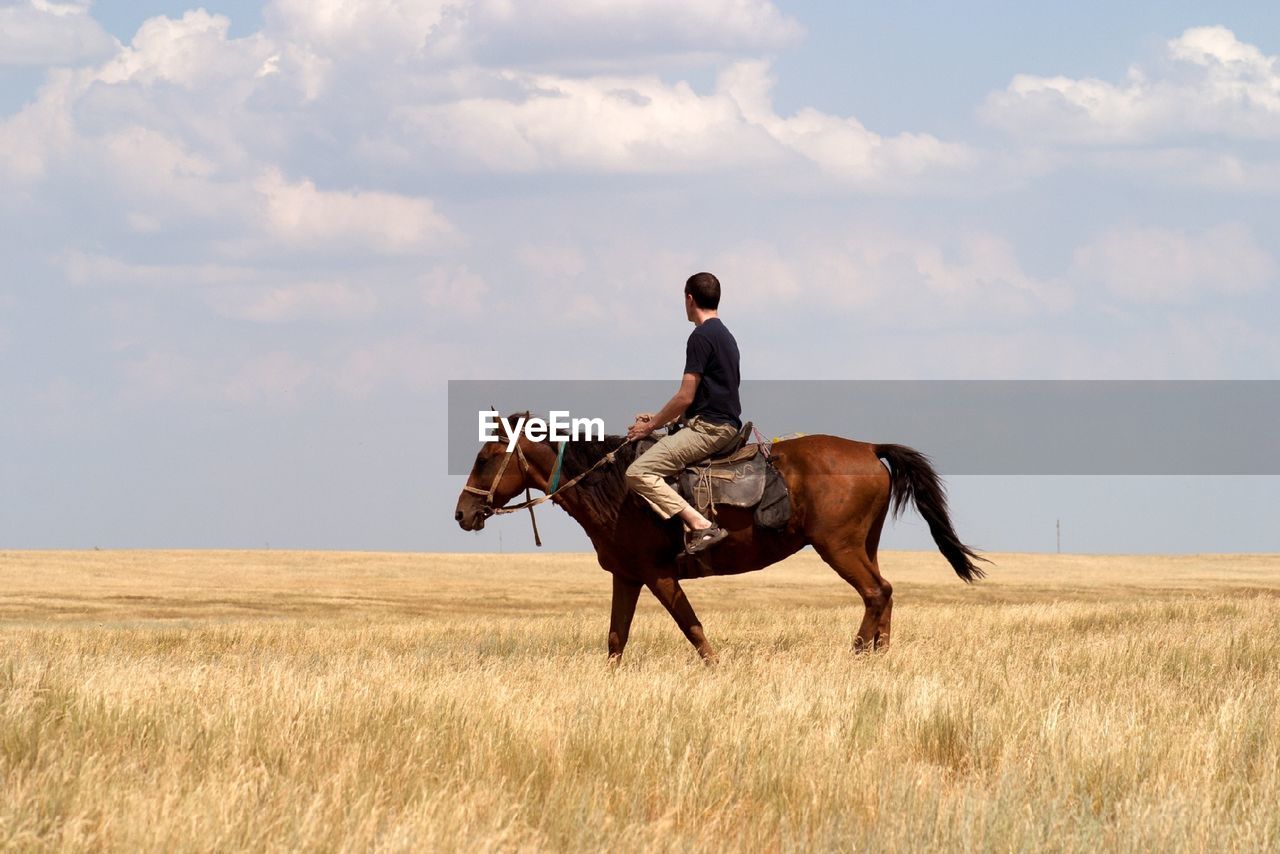 Portrait of man riding horse on field against cloudy sky