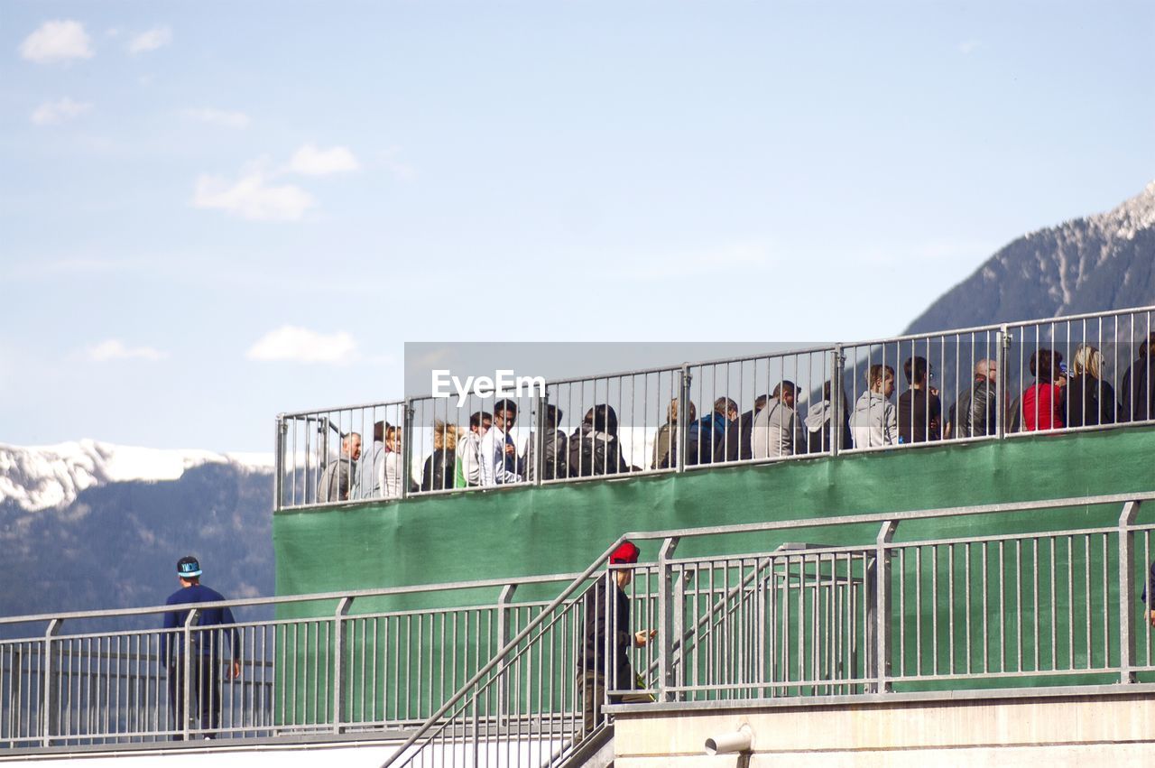 Low angle view of people at soccer stadium by mountains against sky