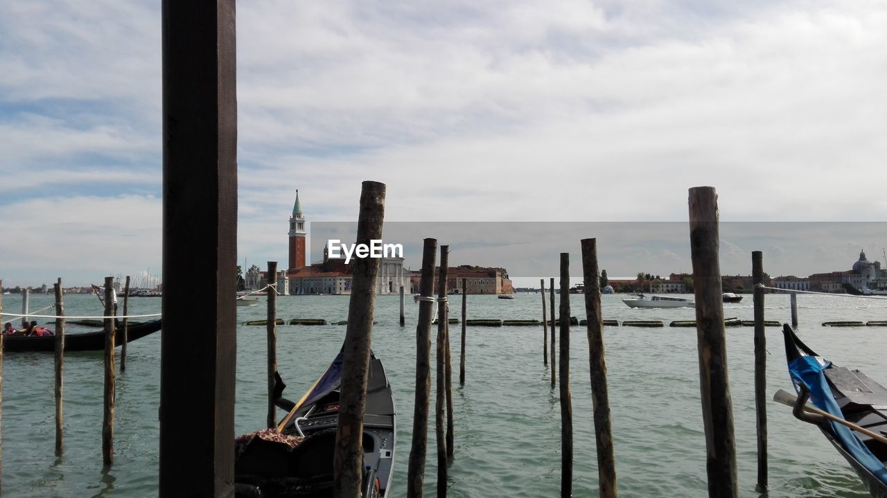 Wooden posts in sea against cloudy sky