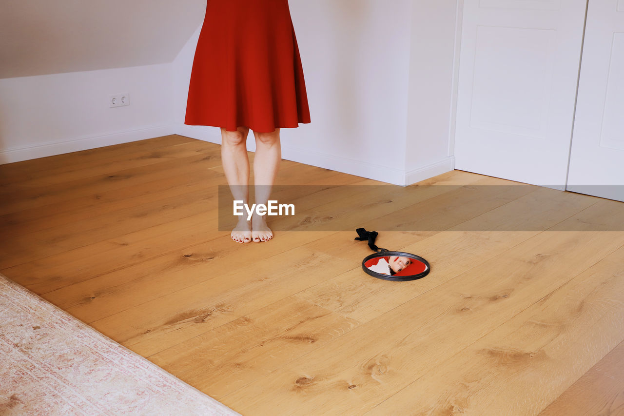 Low section of woman standing by mirror on hardwood floor