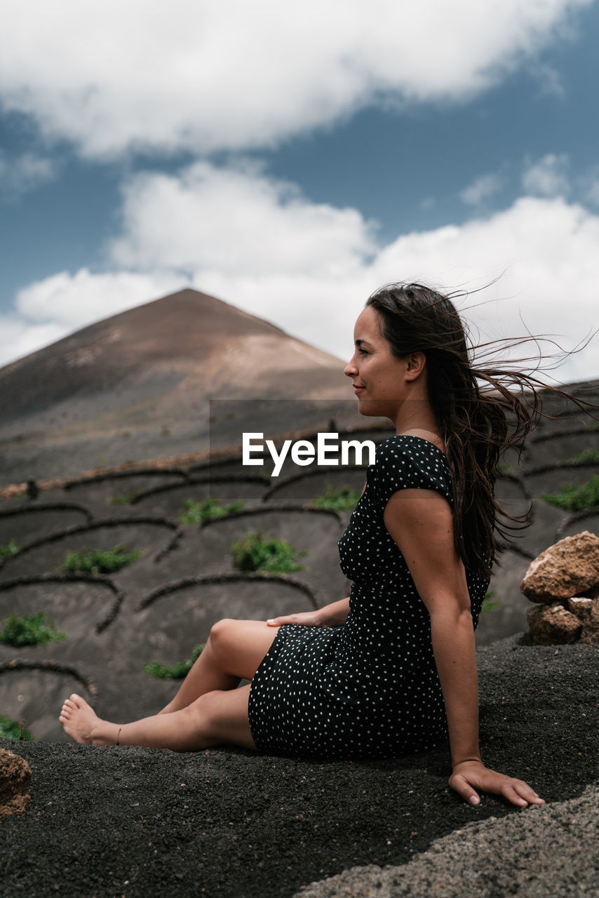 Beautiful young woman sitting on land against sky