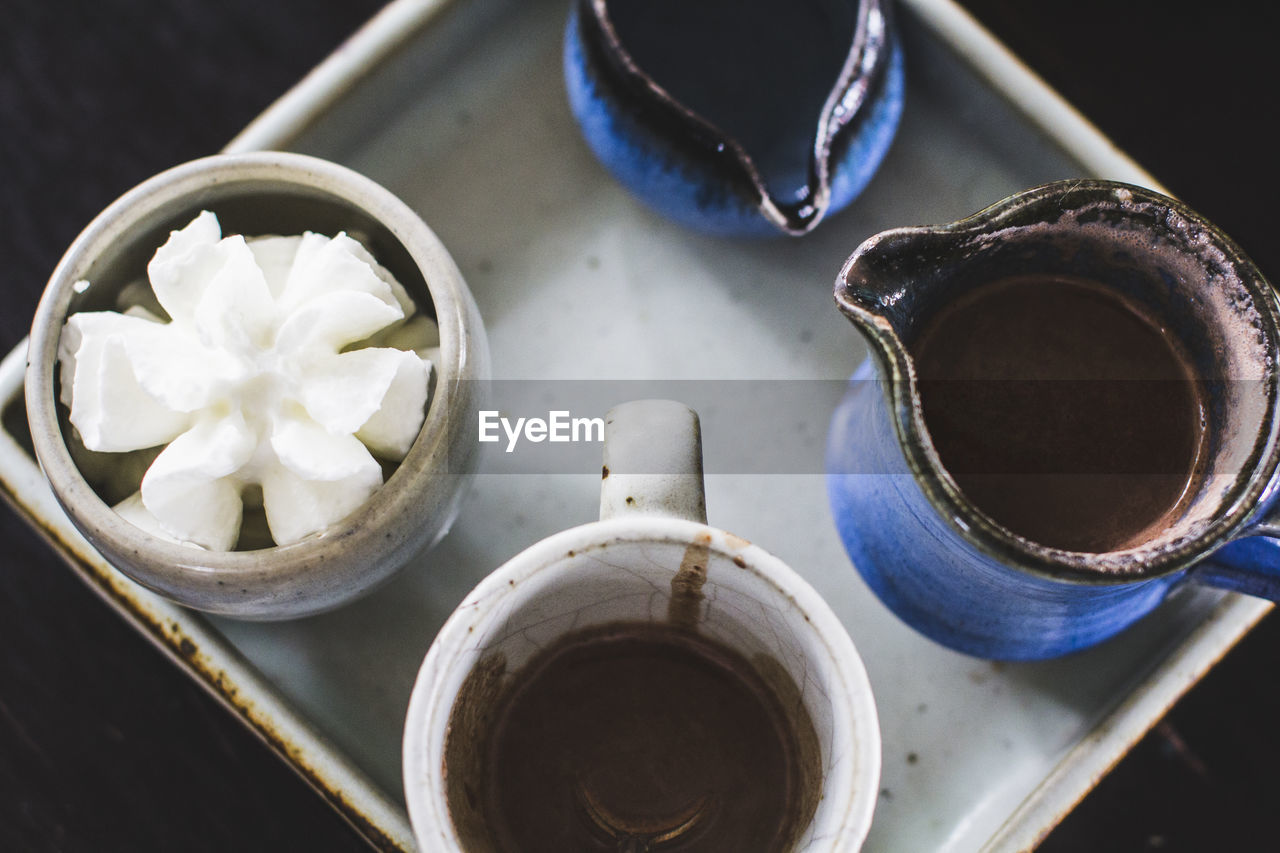 High angle view of hot chocolate in pitcher with cream on tray