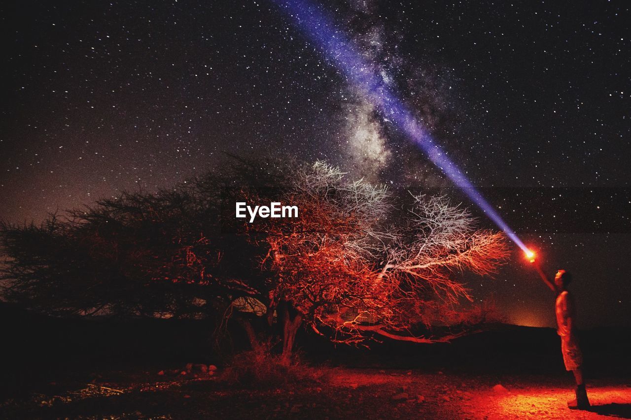 Man with flashlight standing on field against star field at night