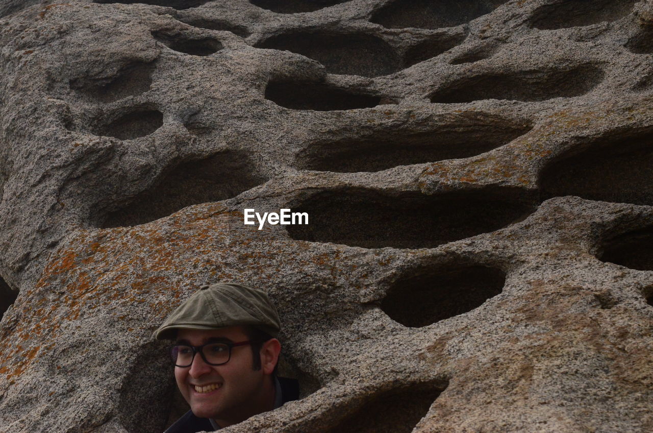 PORTRAIT OF SMILING YOUNG MAN ON ROCK WITH FACE