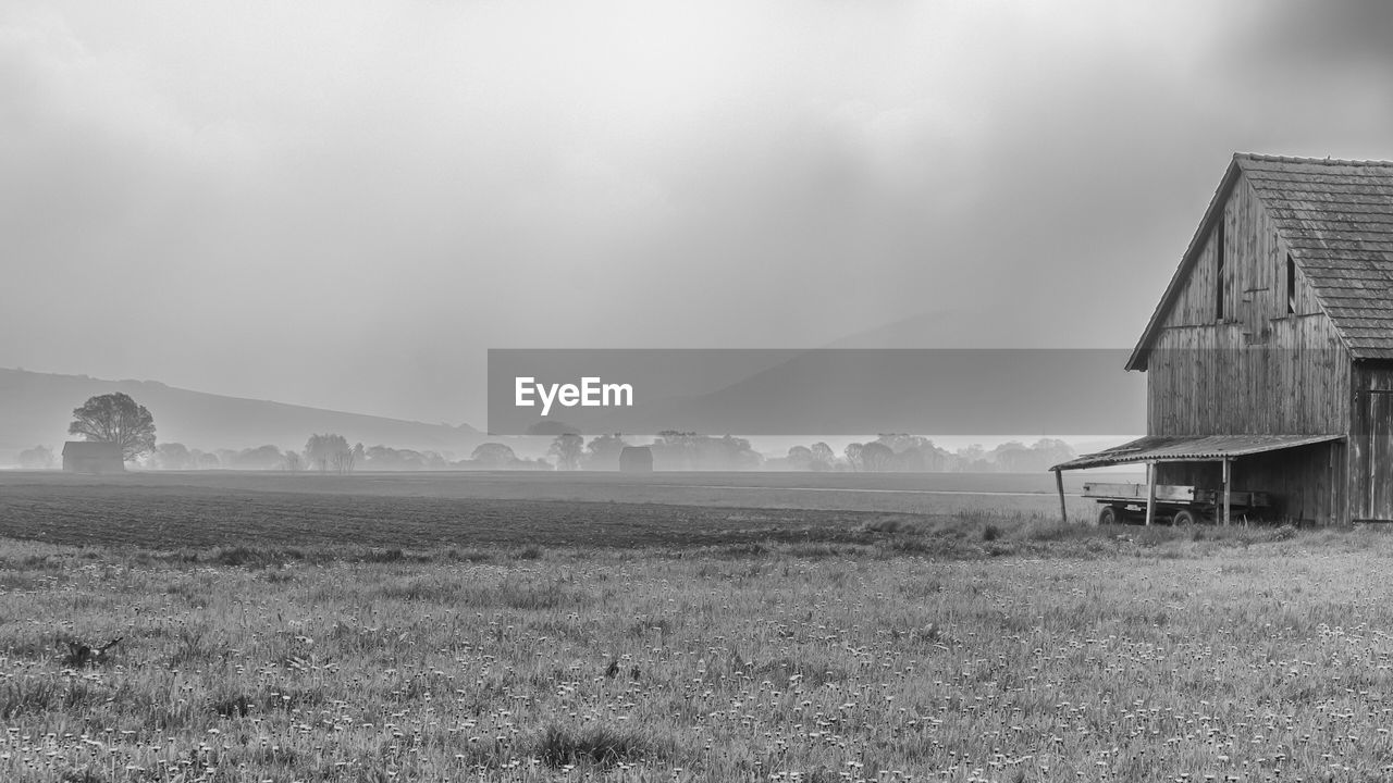 BARN ON FIELD BY MOUNTAIN AGAINST SKY