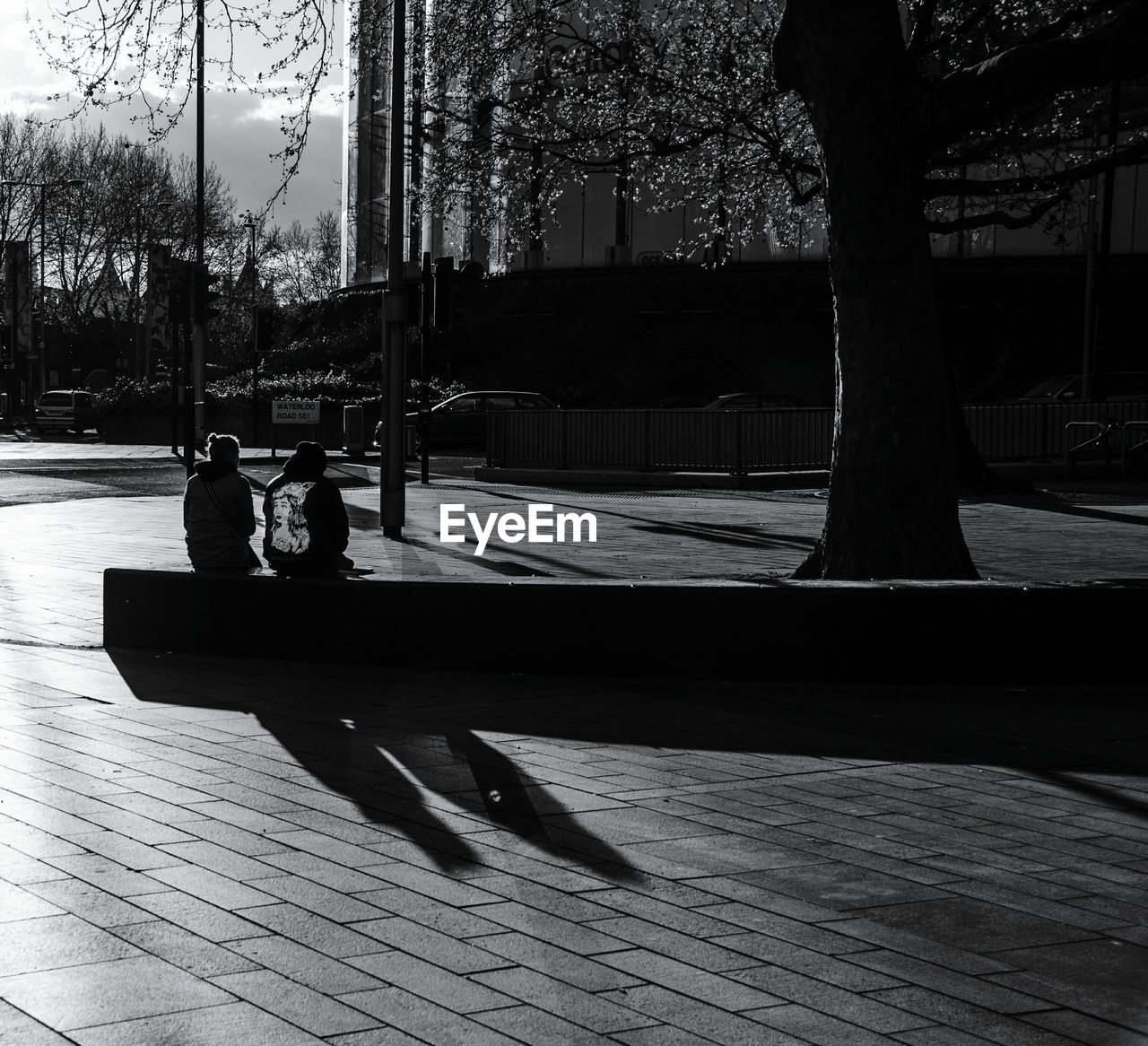 Men and woman sitting on concrete bench by road in city