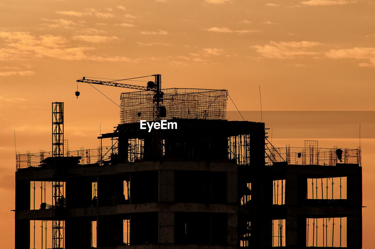 LOW ANGLE VIEW OF SILHOUETTE CRANES ON BUILDING AGAINST SKY