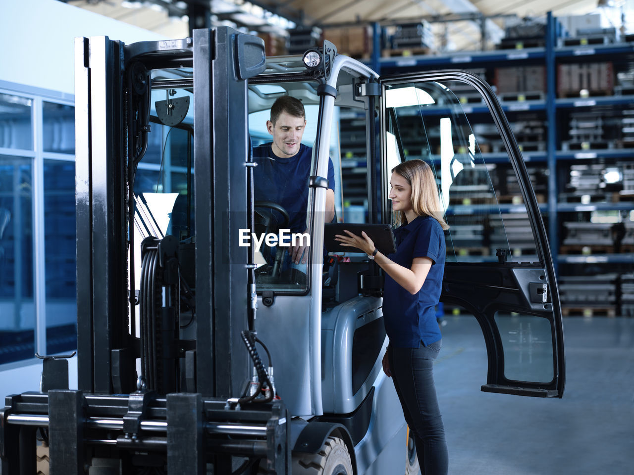 Engineer showing tablet pc with worker in forklift at factory