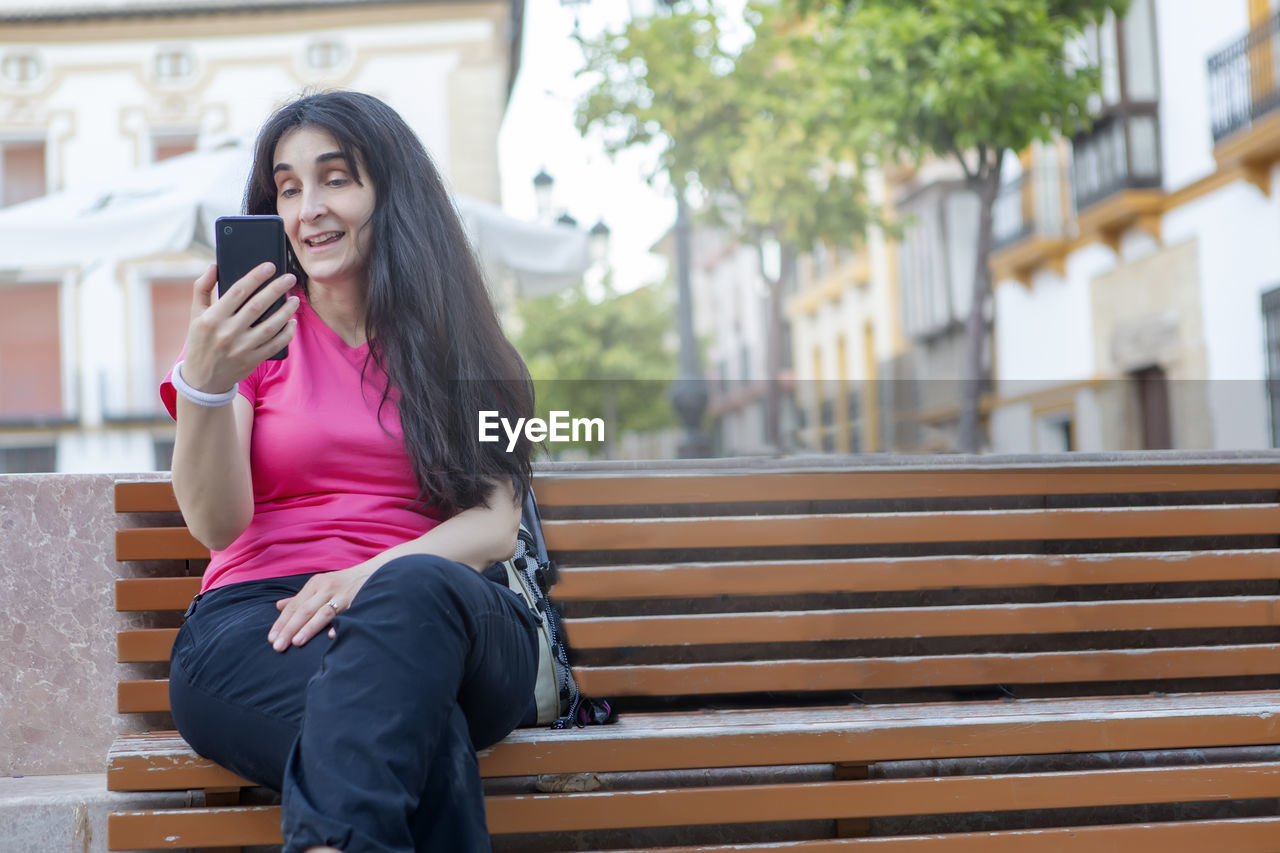 Young lifestyle city people sitting on a street bench using their mobile phone on video call. 