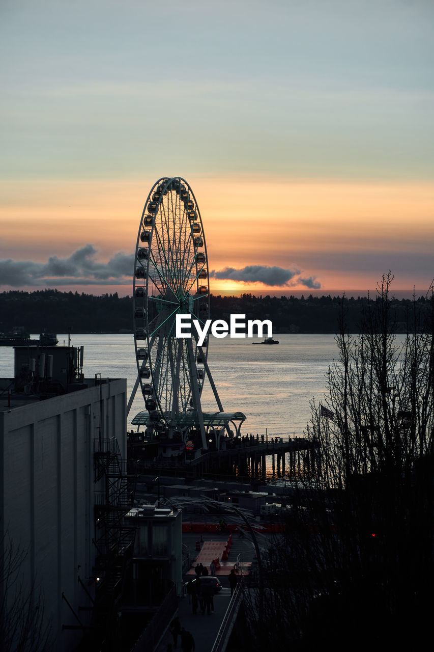 sky, sunset, amusement park ride, amusement park, ferris wheel, water, architecture, evening, nature, built structure, dusk, cloud, reflection, arts culture and entertainment, no people, travel destinations, outdoors, sea, roller coaster, silhouette, night, transportation, tree