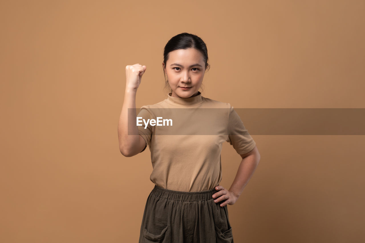 studio shot, one person, portrait, adult, colored background, indoors, looking at camera, standing, young adult, front view, copy space, emotion, smiling, photo shoot, brown, t-shirt, three quarter length, hand, happiness, clothing, sleeve, gesturing, men, waist up, arm, person, casual clothing, brown hair, beige background, cut out, finger