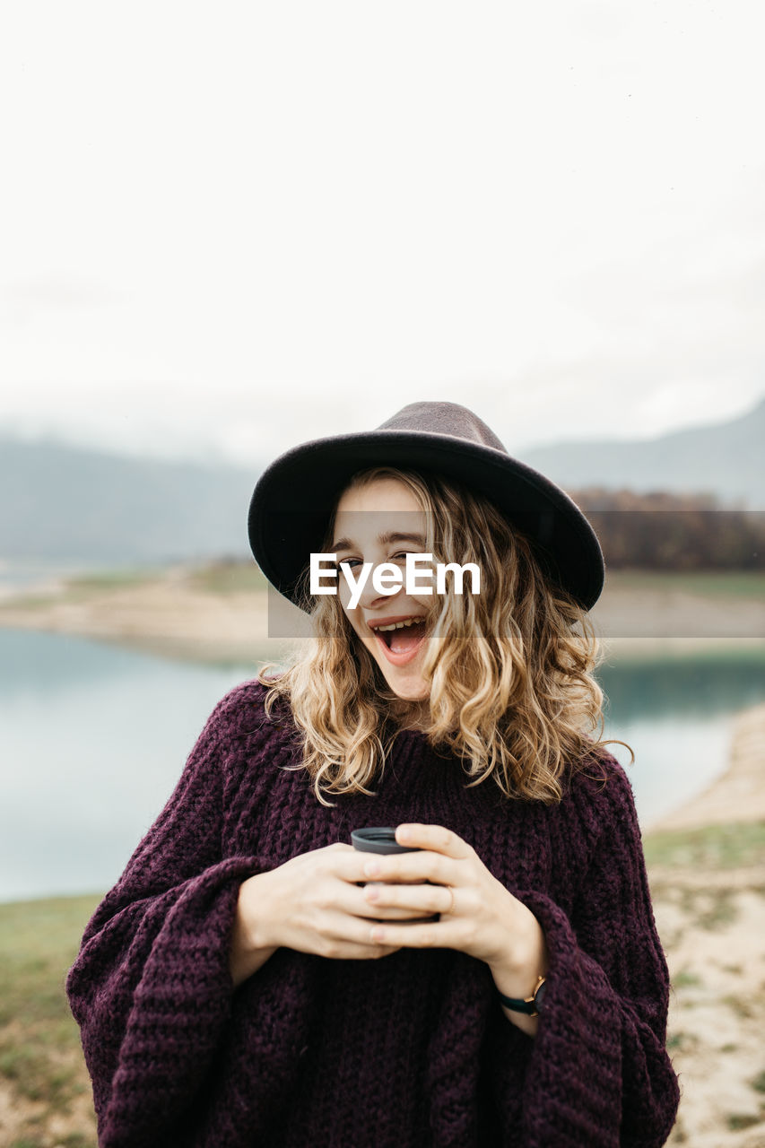 BEAUTIFUL YOUNG WOMAN USING PHONE WHILE STANDING ON SHORE