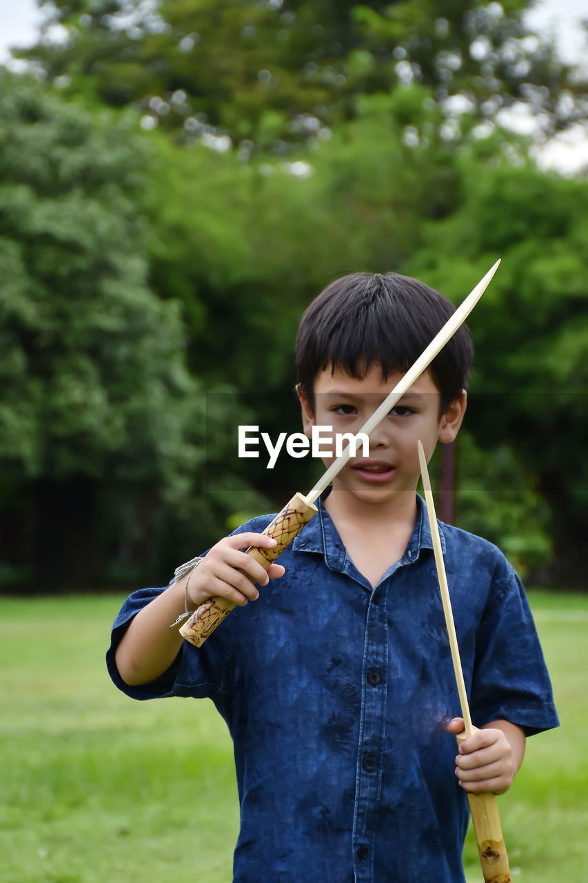 Boy holding wooden equipment while standing outdoors